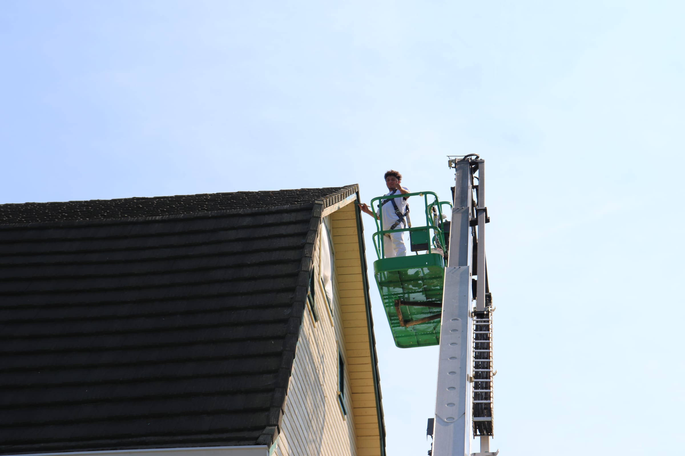 Boom lift raised above the roof peak of a large building with a painter in the basket