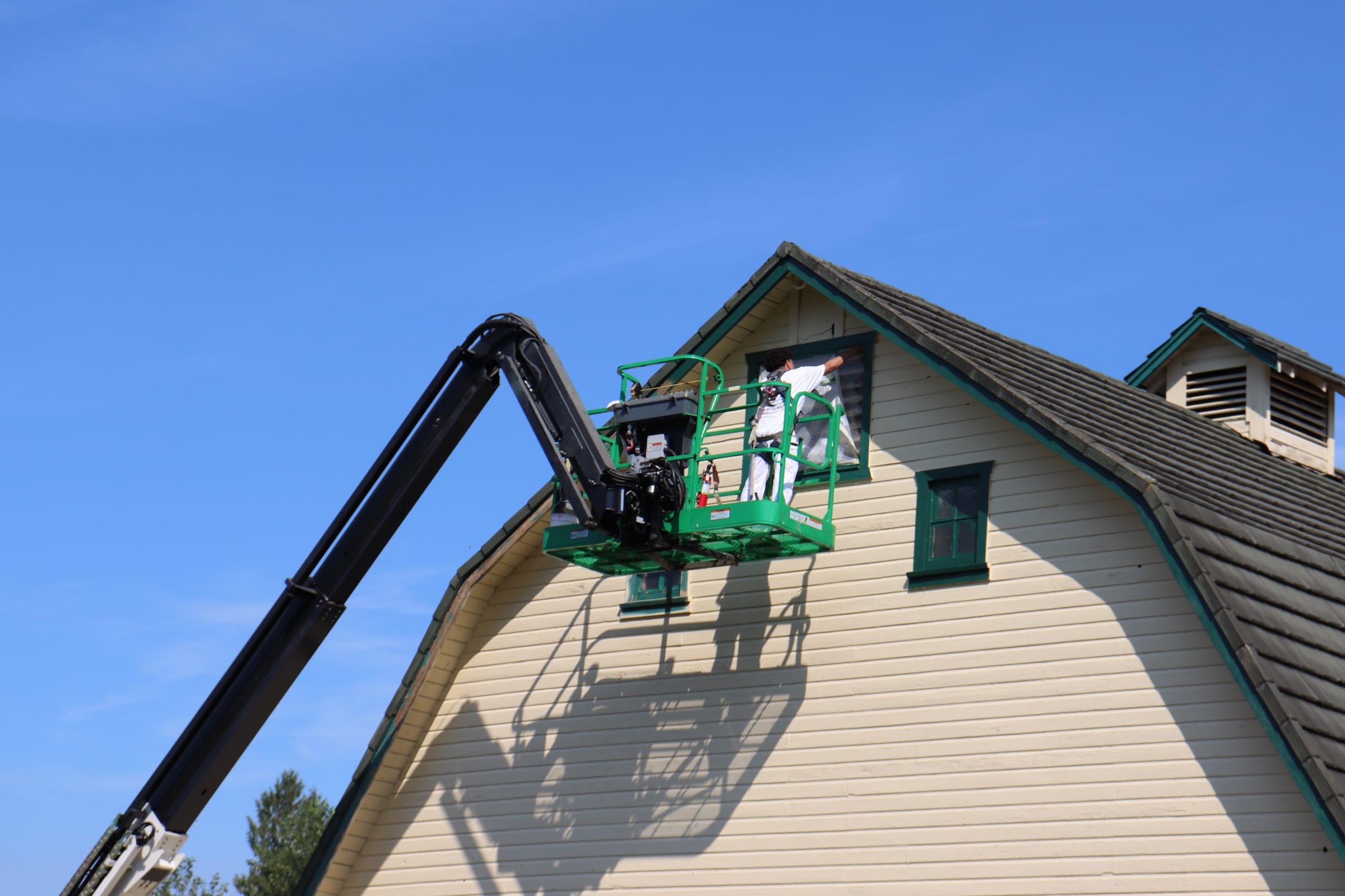 Boom lift positioned against the gambrel end wall of a barn during an exterior repaint