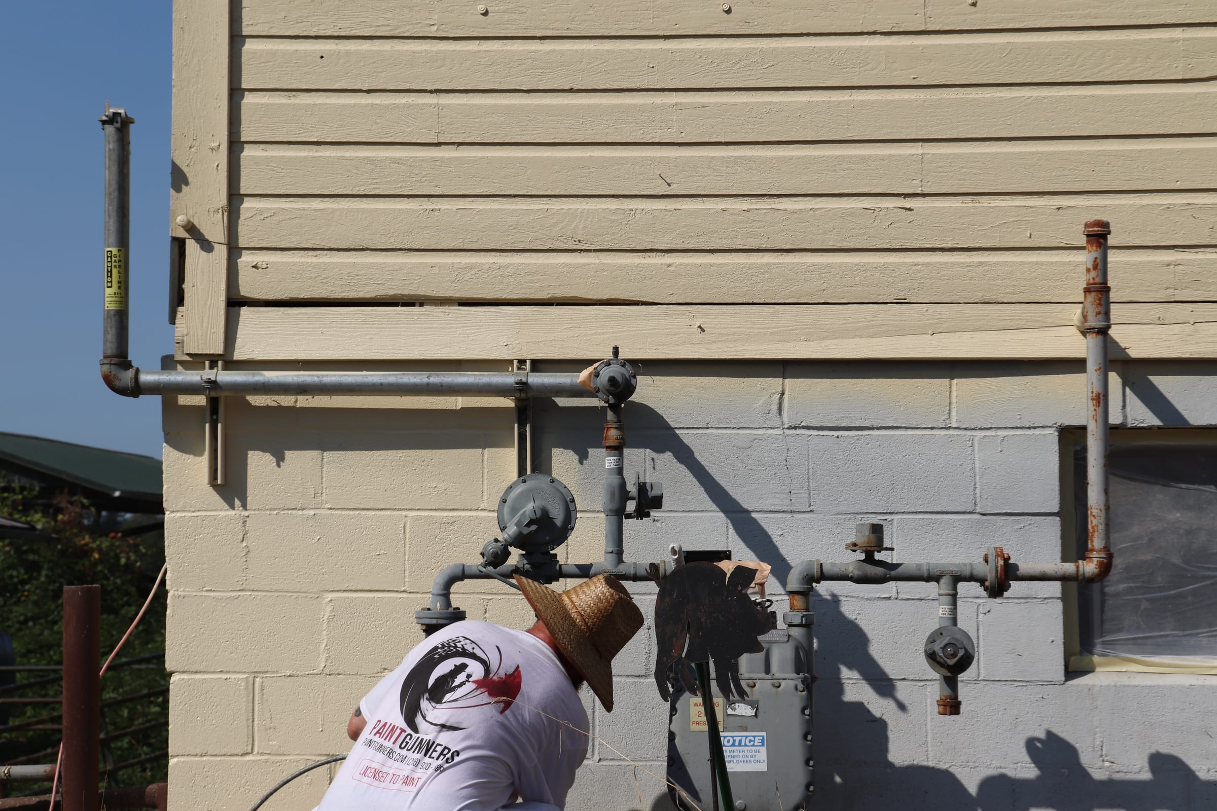 Painter working carefully around exterior gas piping and a meter on a block wall